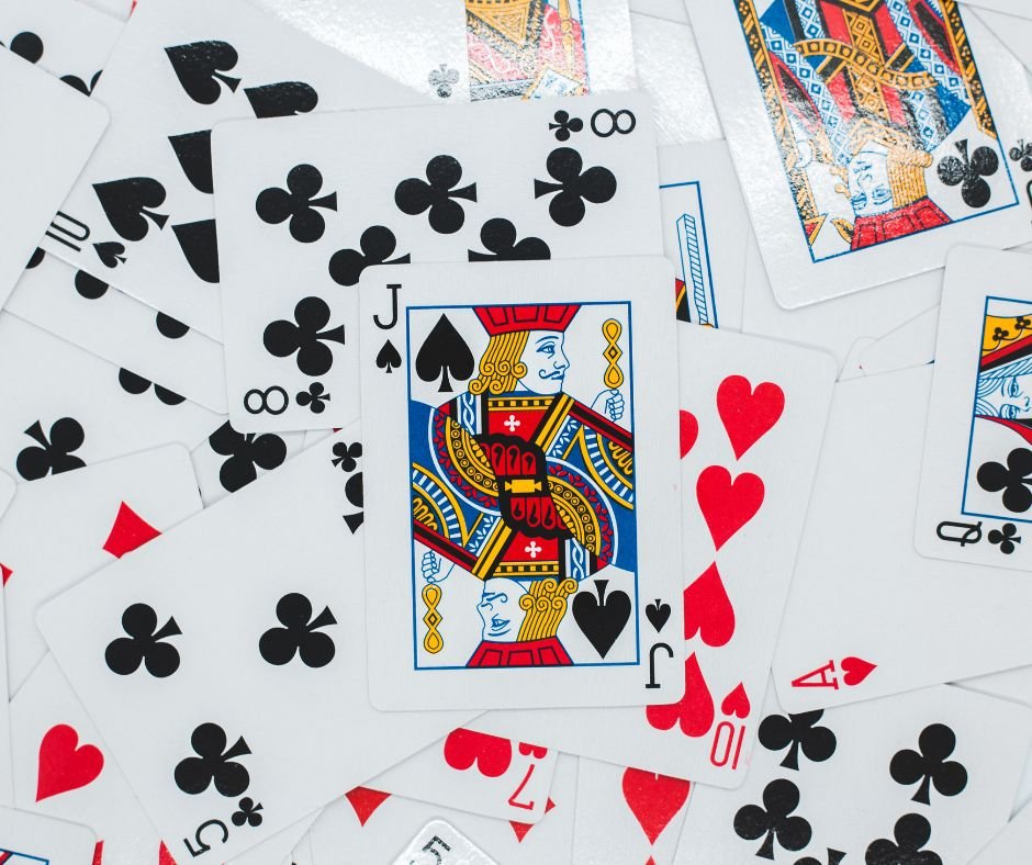 A scattered pile of playing cards featuring various suits, with a prominent jack of spades in the center, reflects the dynamic art of outsourcing for business efficiency—just like a virtual assistant skillfully managing tasks.